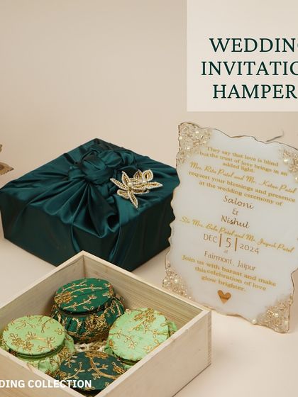 A complete wedding invitation set, featuring a custom acrylic invite, a wooden box filled with small embroidered gift pots, and a larger gift wrapped in luxurious teal fabric.