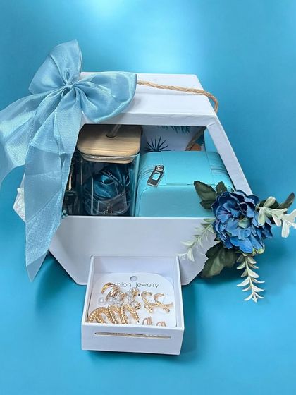 A beautiful gift hamper for her in shades of blue, presented in a unique hexagonal white box with a drawer. It includes jewelry and other curated items, tied with a large blue bow.