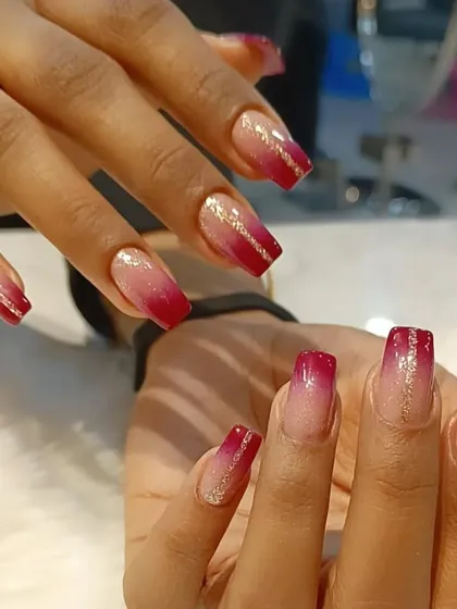 A beautiful red ombre on coffin nails, fading from light to dark and accented with a delicate line of gold glitter.