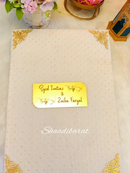The cover of a custom Nikah booklet in a soft cream color with gold accents. The couple's names are elegantly displayed on a gold acrylic plate.