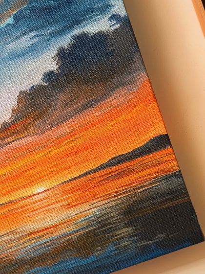 Another angle of the vibrant orange sunset painting, showing the texture of the canvas and the detailed cloud formations.