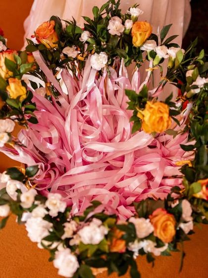 A basket decorated with a ring of fresh flowers and filled with pink ribbons, likely for a game or guest activity during the Mehendi.