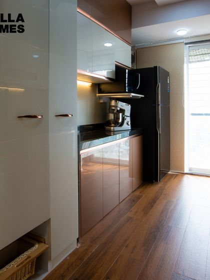 This parallel kitchen for the Kazi family features a beautiful combination of glossy white and rose-gold cabinets with wooden flooring.
