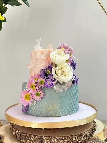 A close-up of a two-tiered anniversary cake. I used a textured buttercream technique in sage green and peach, with a cascade of fresh flowers and delicate rice paper sails for a modern, artistic look.