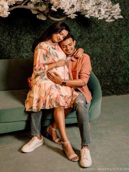A sweet and tender portrait of an expecting couple on a green sofa. The focus is on their happy expressions and the gentle way they hold the baby bump.