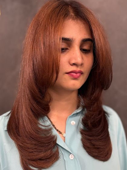 A portrait of the client, her copper hair styled with face-framing bangs and soft, feathered ends.