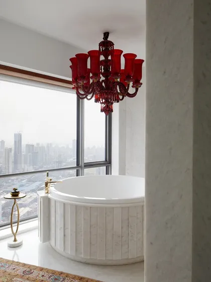 In this master bathroom high above the Mumbai skyline, luxury meets drama. A vintage red Murano glass chandelier hangs over a custom marble spa bath, creating a romantic and intensely personal retreat with an unparalleled view of the city.
