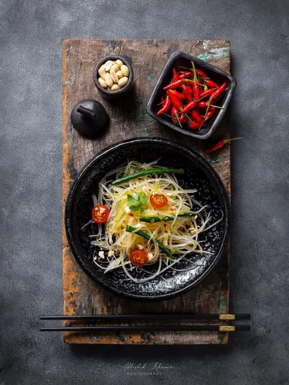 A top-down, moody shot of a Som Tam salad, styled on a rustic wooden board for Fairmont Jaipur.