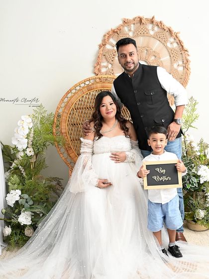A bright and happy family maternity photo. The son holds a "Big Brother" sign, sharing the happy news in this light-filled boho-themed session.
