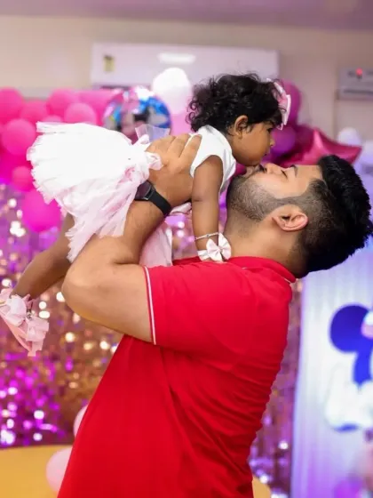 A heartwarming shot of a father lifting his daughter up in the air at her brightly decorated birthday party.