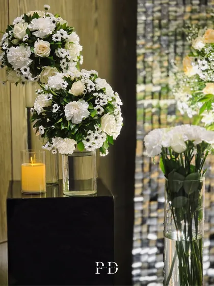 Elegant floral arrangements in tall glass vases, paired with candles, create a clean and classic look for a glamorous indoor event.