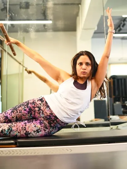 A client holds a graceful side-lying pose on the reformer, using a push-through bar for support. This move strengthens the obliques and improves lateral flexibility of the spine.