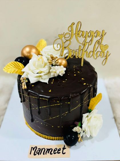 A classic chocolate truffle cake with a glossy drip, gold accents, and elegant white roses. A sophisticated choice for any celebration.