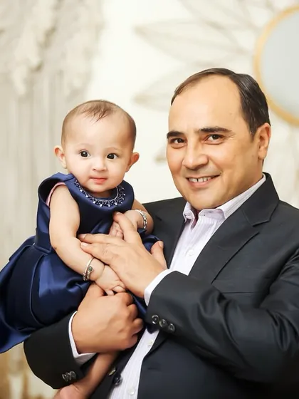 A proud father holding his beautiful baby girl. This classic portrait showcases the special bond between a dad and his daughter in a simple, elegant studio setting.