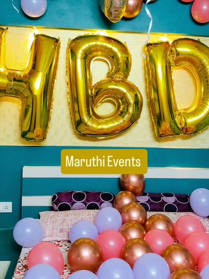 A simple 'HBD' surprise on a bed, using large gold foil letters and pastel-colored balloons.