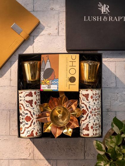 A top-down view of our 'Divine' Diwali hamper. This gift set includes patterned tumblers, a lotus-shaped diya, and incense, all beautifully arranged in our signature black box.