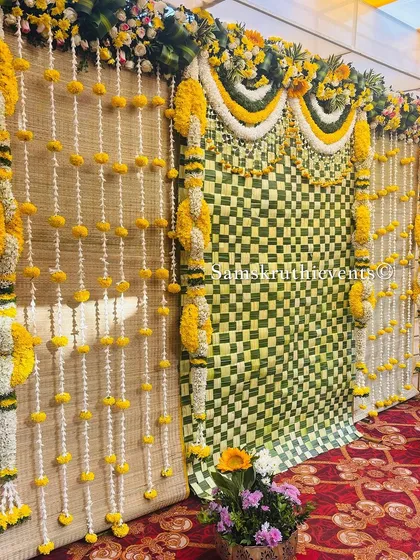 A side view of a traditional backdrop, showing the combination of woven mats and a checkerboard pattern of leaves. The hanging marigold garlands complete this rustic and authentic look.