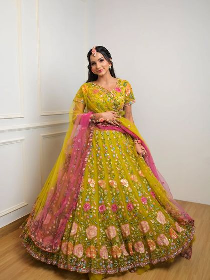 A full-length shot of the bride in her stunning yellow and pink lehenga. The makeup complements the vibrant colors of her outfit perfectly.