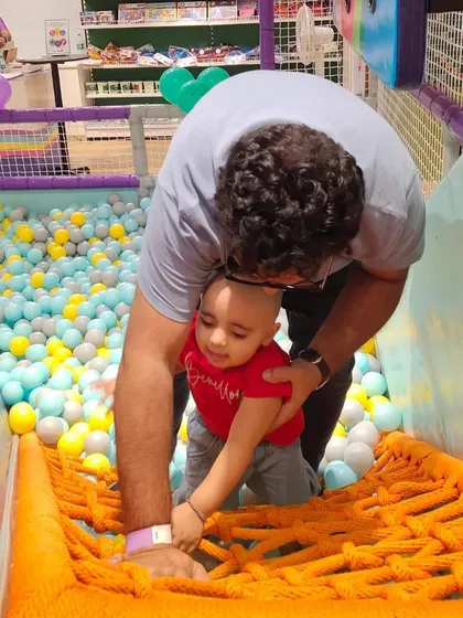 One step at a time. A parent helps their toddler navigate a rope bridge, a special moment of encouragement.