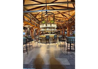 A wide shot of the bar and lounge area at KGA. The design uses natural materials like wood and stone, complemented by lush greenery, to create a space that feels both luxurious and grounded in nature.