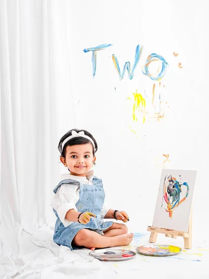 A quiet moment amidst the creative chaos. This little artist sits proudly with her masterpiece during her paint-themed second birthday photoshoot.