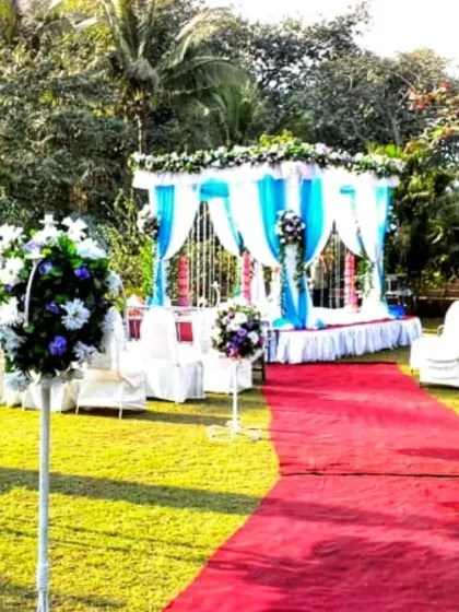A picturesque garden wedding mandap with blue and white drapes, white seating for guests, and a red carpet aisle leading to the ceremony area.