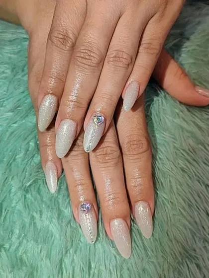 A glamorous set of long, stiletto nails with a shimmery nude base and large crystal accents.