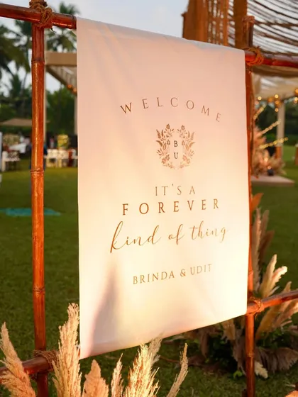 A personalized welcome sign for a boho Sangeet, with the message "It's a forever kind of thing". The simple typography and custom monogram on a fabric banner add a touch of rustic elegance.