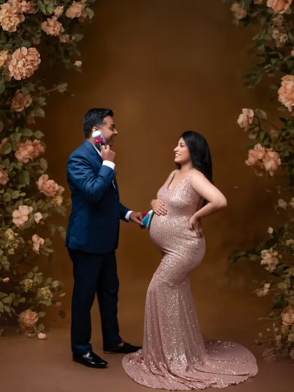 A playful moment during a glamorous shoot. The father-to-be holds up a pair of baby shoes, bringing a touch of fun to this elegant portrait.