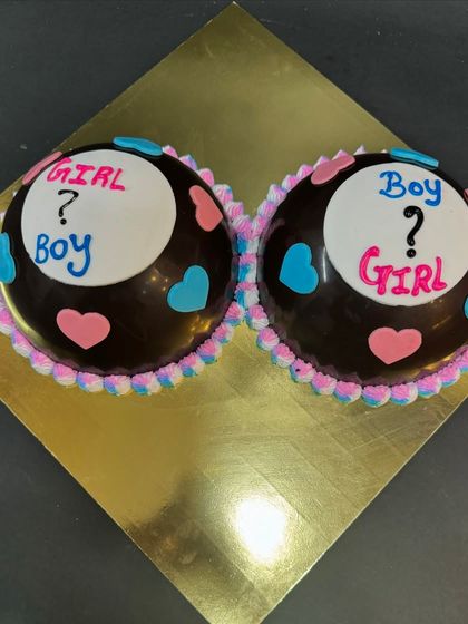 A creative piñata cake for a baby shower. Two chocolate domes are decorated with a "Boy or Girl?" theme, making the gender reveal a fun and delicious surprise.