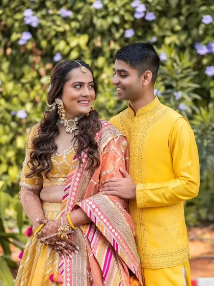 A collection from a beautiful Haldi ceremony. The bride's makeup is fresh and minimal, with a pop of color on the lips. Her hair is styled in a half-up, half-down look with braids, perfect for the fun and vibrant event.
