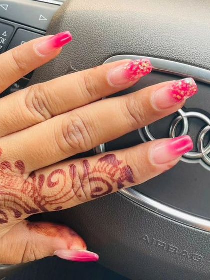A bright pink ombre with a touch of glitter on the tips, shown against the client's beautiful henna design.