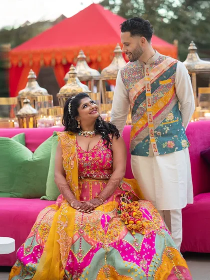 The groom's vibrant, patchwork Nehru jacket coordinates perfectly with the bride's colorful lehenga, creating a look that is both fun and fashionable.