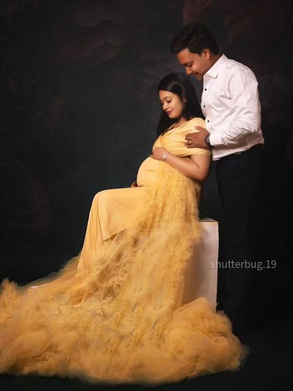 A tender moment between a couple during their maternity session. The mom-to-be is seated in a beautiful yellow gown while her partner stands beside her, creating a classic and loving portrait.