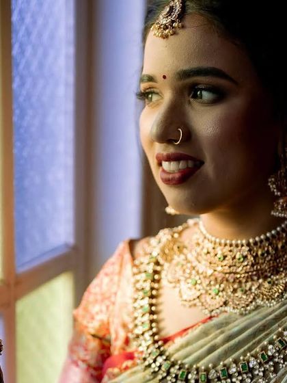 A close-up of a bride looking out a window. The soft, natural light beautifully illuminates her face and traditional jewelry.