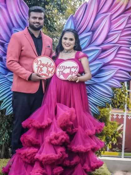 A duplicate of image 4, this photo shows a couple posing with "Daddy To be" and "Mommy To be" signs in front of a large, colorful angel wings prop, creating a fun and whimsical announcement.