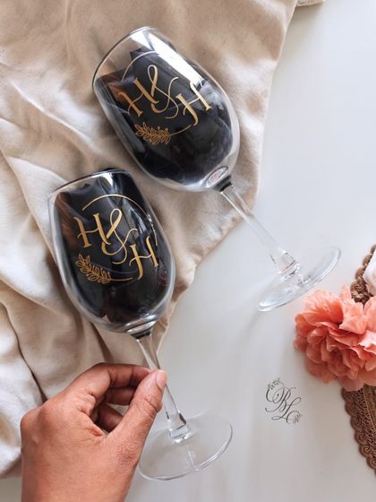 A pair of wine glasses featuring a custom 'H&H' monogram, intertwined with delicate foliage. This design is perfect for a wedding or anniversary, symbolizing two lives joining together.