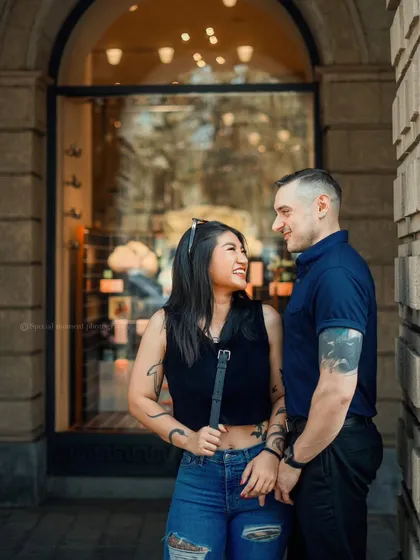 A lovely shot of a couple sharing a look outside a city storefront. The warm lighting and their smiles create a cozy, romantic atmosphere.