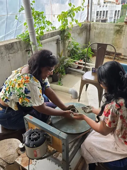 Two participants share a laugh while one learns to use the pottery wheel on our green rooftop terrace. The vibe is always friendly and supportive.