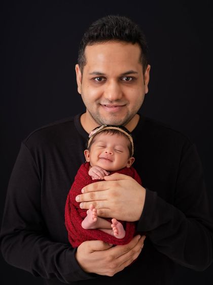 A proud father holding his smiling newborn. The joy on his face is a perfect match for the baby's sweet, sleepy smile.