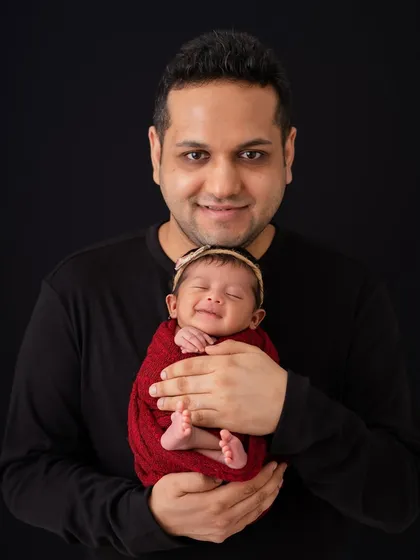 A proud father holding his smiling newborn. The joy on his face is a perfect match for the baby's sweet, sleepy smile.