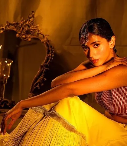 A beautiful, moody portrait of a bride in a yellow lehenga. The makeup is soft and luminous, with a traditional headpiece, creating a timeless and artistic bridal image.