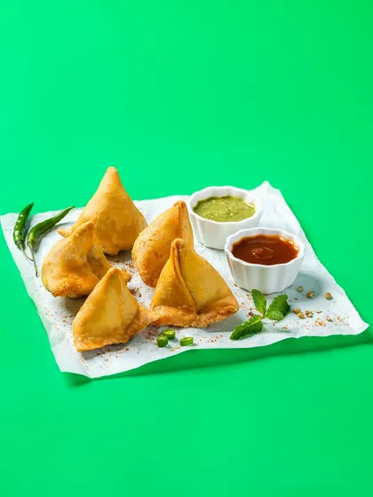 Crispy samosas with chutneys, shot against a vibrant green screen for Bistro by Blinkit. This style is perfect for e-commerce platforms and apps, allowing for easy background removal and consistent branding.