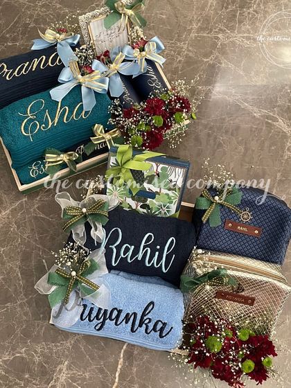 We create unique hampers that blend practicality with sentiment. This display shows two distinct couple sets, one in blue and green tones and another in blue and gold, each with personalized towels and matching accessories.