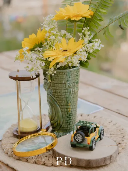 A close-up of the safari-themed table centerpiece, featuring a miniature jeep, an hourglass, and yellow gerberas. These small, thematic details bring the entire concept to life.
