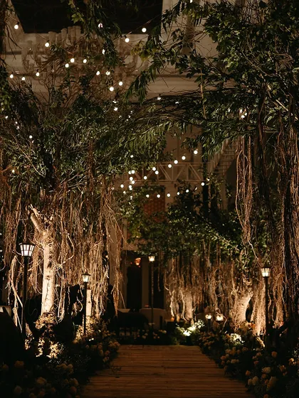 An enchanted forest theme for a Sangeet night. The pathway is lined with majestic trees and fairy lights, creating a magical and immersive experience for guests as they enter the venue.