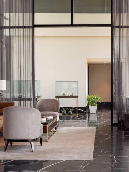 This wide shot of the lounge area shows how we use full-height glass and sheer curtains to maintain a connection to the outdoors while creating a sense of privacy. The combination of metallic accents, plush fabrics, and a polished marble floor exudes modern luxury.