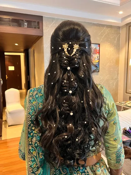 Soft and sophisticated curls for a touch of romance. This intricate hairstyle features braids and waves, decorated with pearls for a glamorous look.
