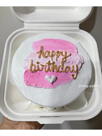 A modern birthday cake design with a pink brushstroke effect and 'happy birthday' written in elegant gold script.