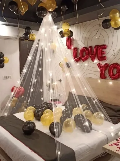 A cozy canopy tent over the bed, decorated with fairy lights and 'I Love You' foil balloons. The black and gold balloons add a touch of elegance.
